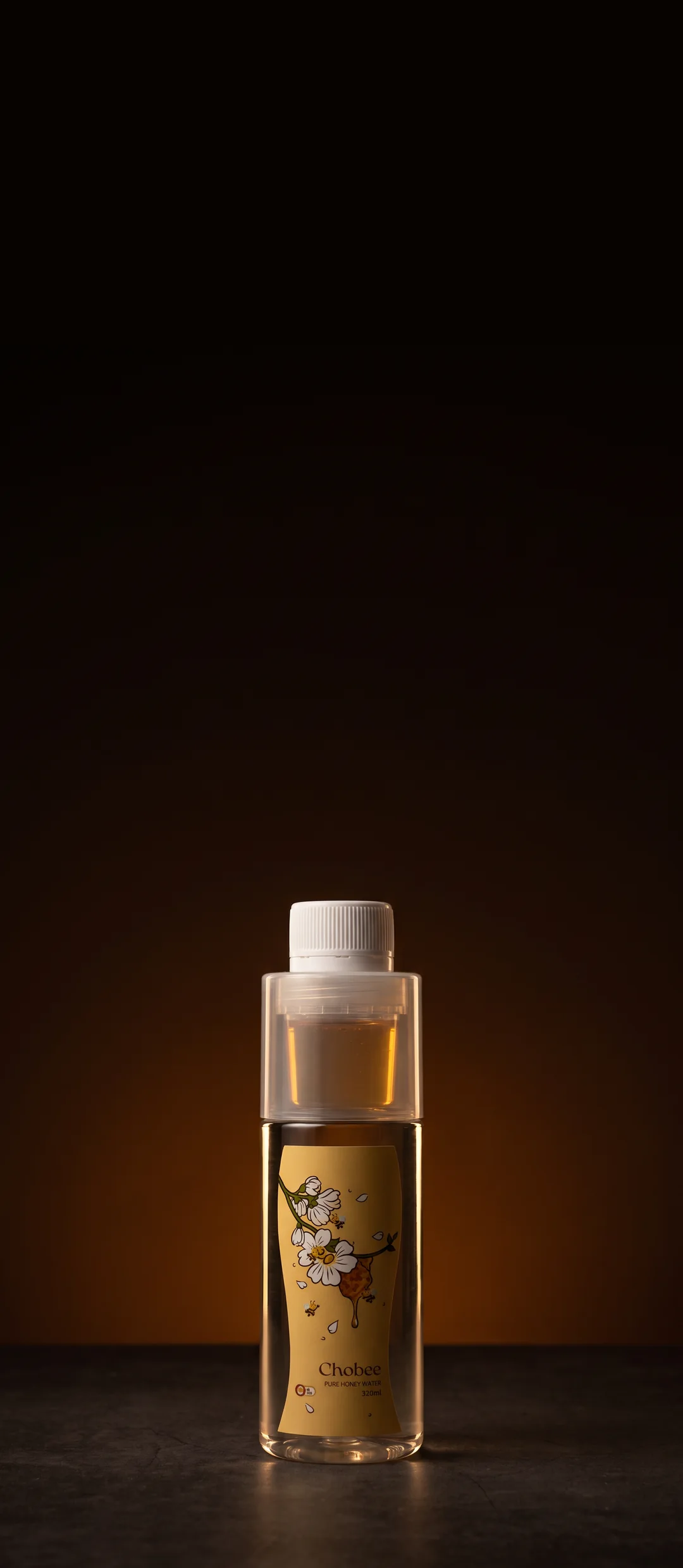 A bottle of CHOBEE Pure Honey Water lit against a deep amber backdrop